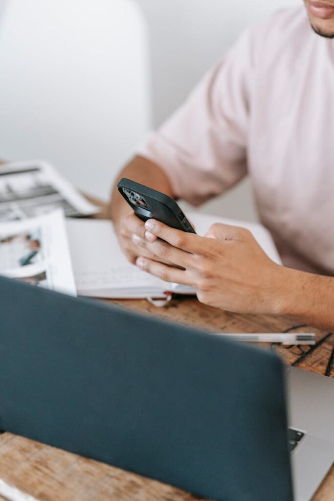 Anonymous man surfing smartphone near laptop